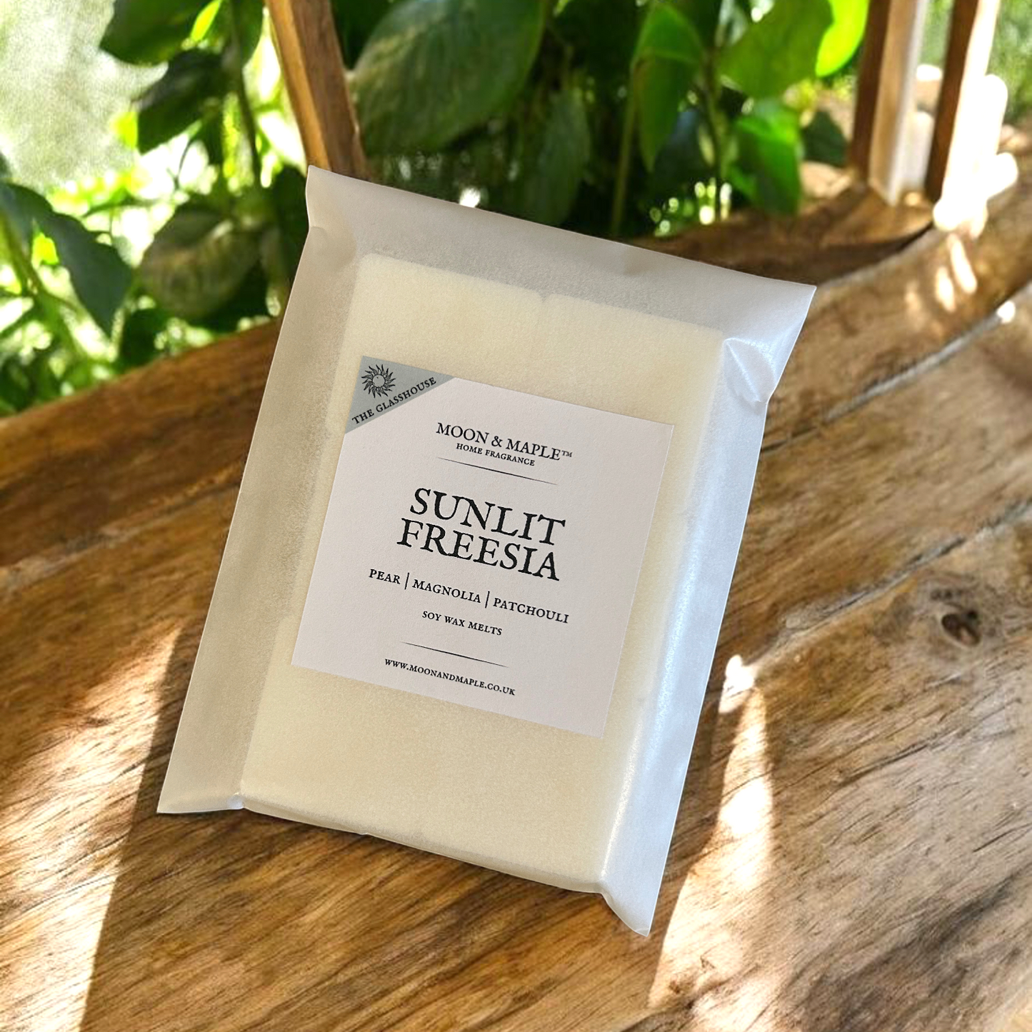Packaged wax melts labeled 'Sunlit Freesia' by Moon & Maple on a wooden surface with greenery in the background.