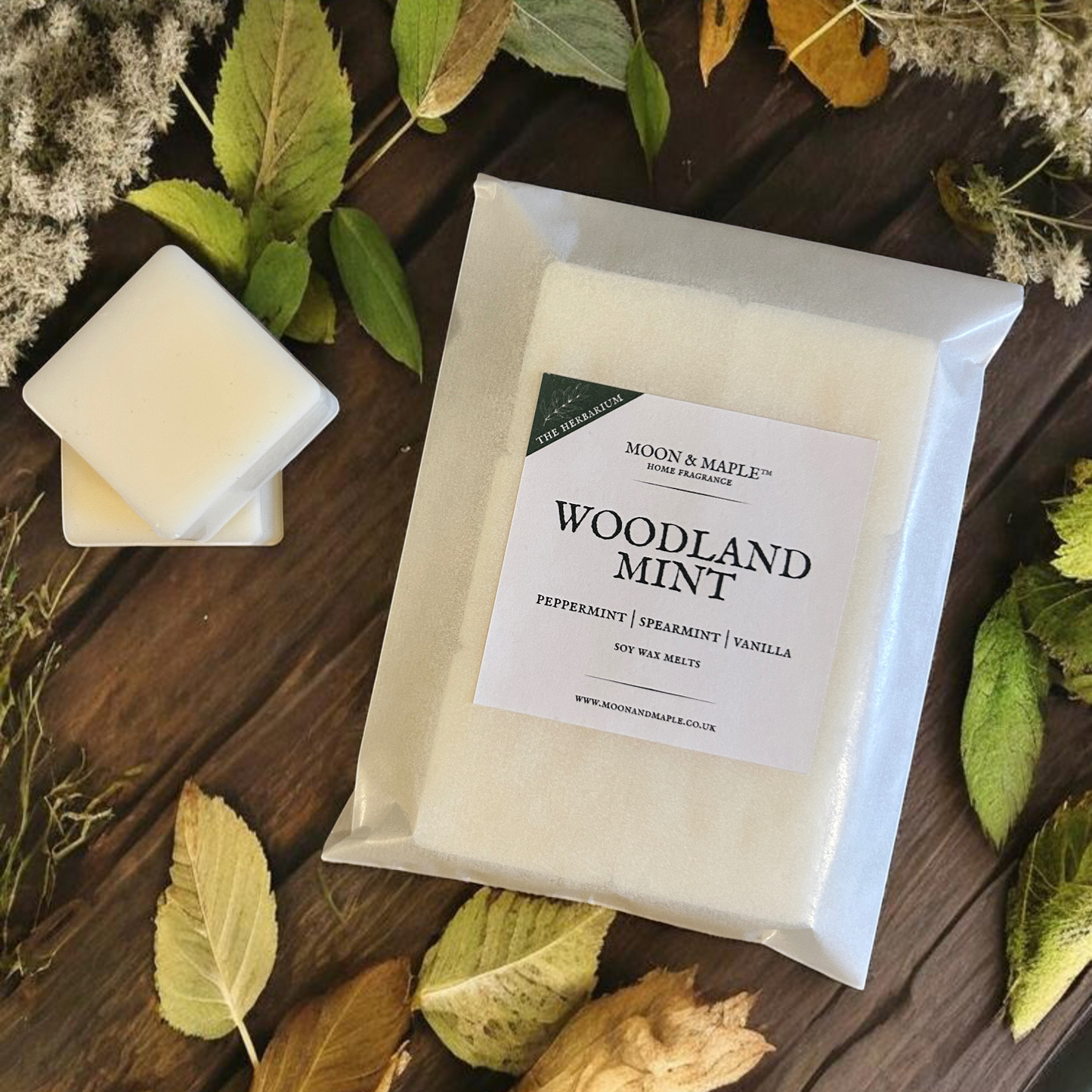 Packaged wax melts labeled 'Woodland Mint' on a wooden surface with leaves.