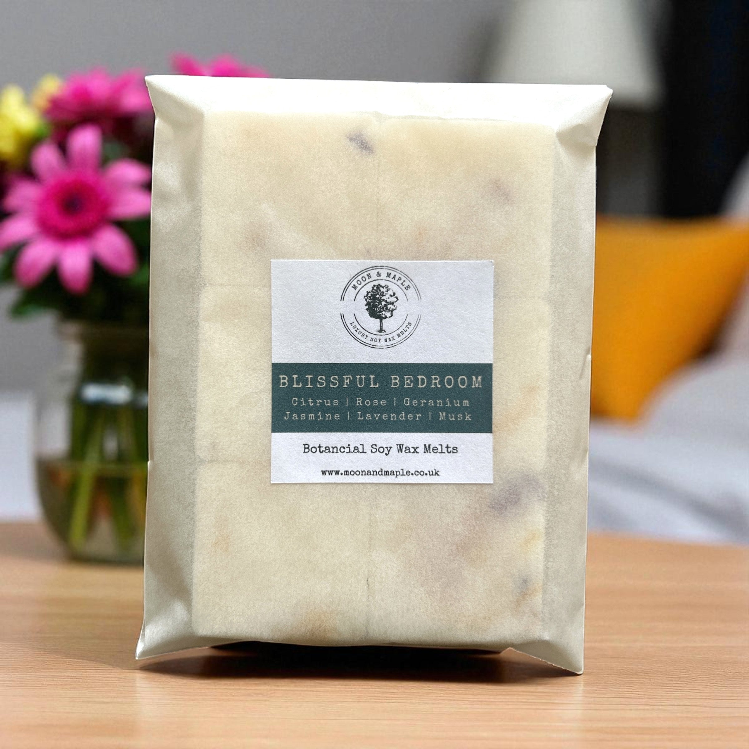 Packaged product labeled 'Blissful Bedroom' on a wooden surface with flowers in the background