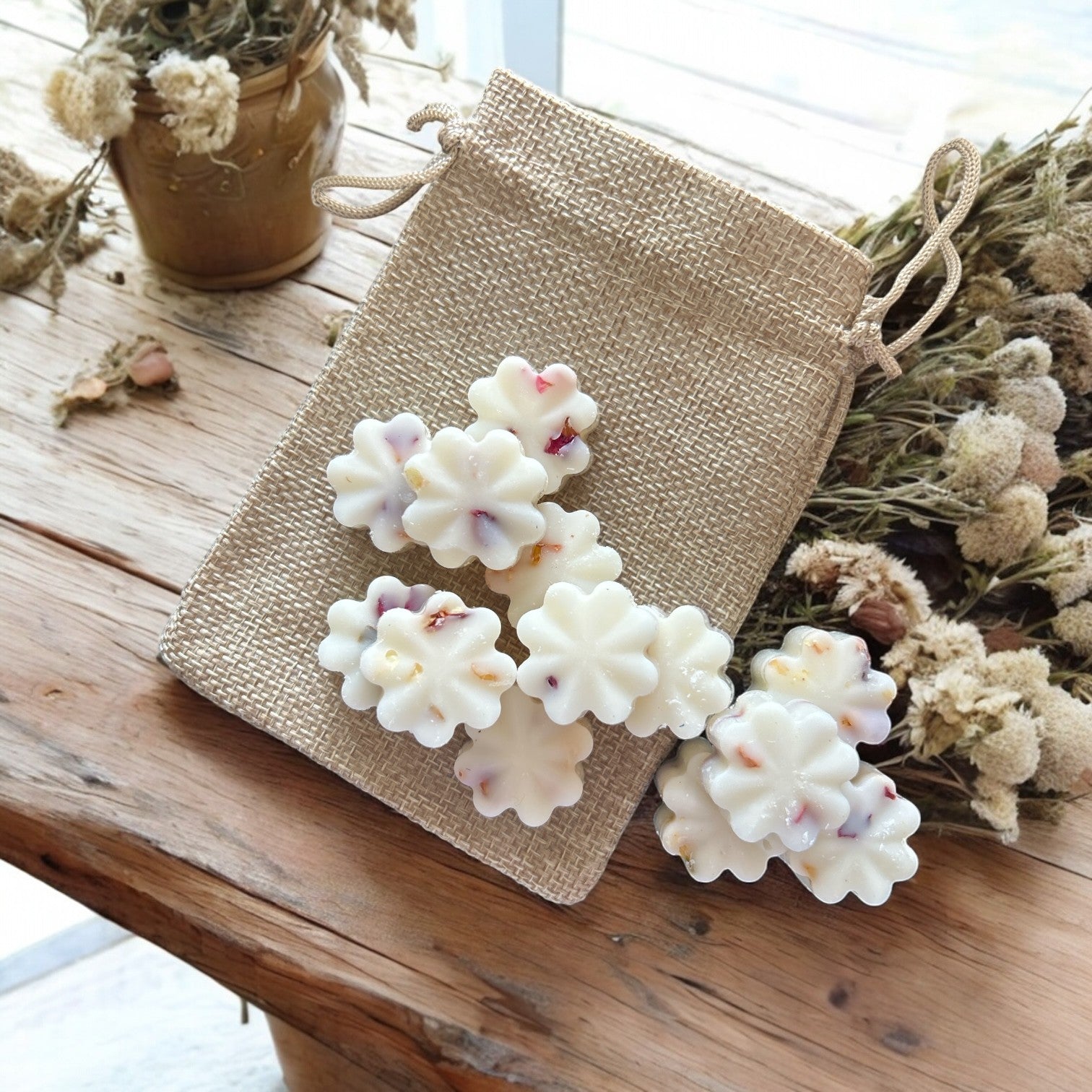 Flower shaped wax melts on a wooden surface with a burlap bag and dried flowers.