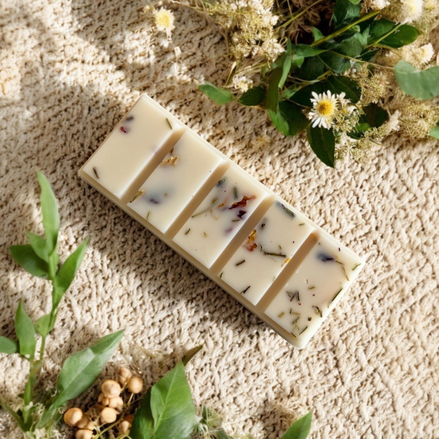 White soy wax snap bar infused with dried botanicals sat on a cream rug and surrounded by dried flowers.