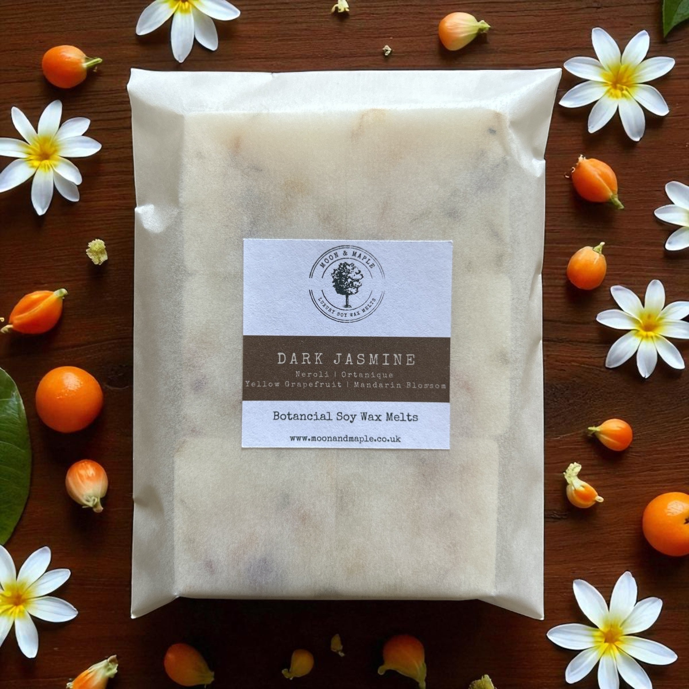 Packaged product labeled 'Dark Jasmine' surrounded by flowers and fruits on a wooden surface