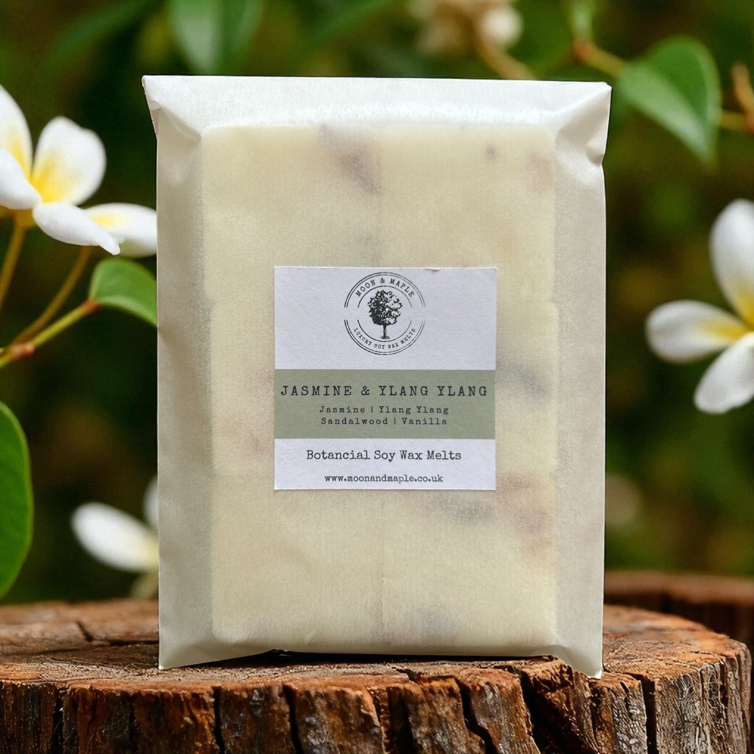 Packaged wax melts labeled 'Jasmine & Ylang Ylang' on a wooden surface with flowers in the background