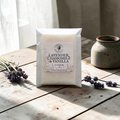 A pack of soy wax melts with a label reading 'LAVENDER, CHAMOMILE & VANILLA' sits on a rustic wooden table. The scene is styled with sprigs of lavender and a speckled ceramic pot in soft natural light.