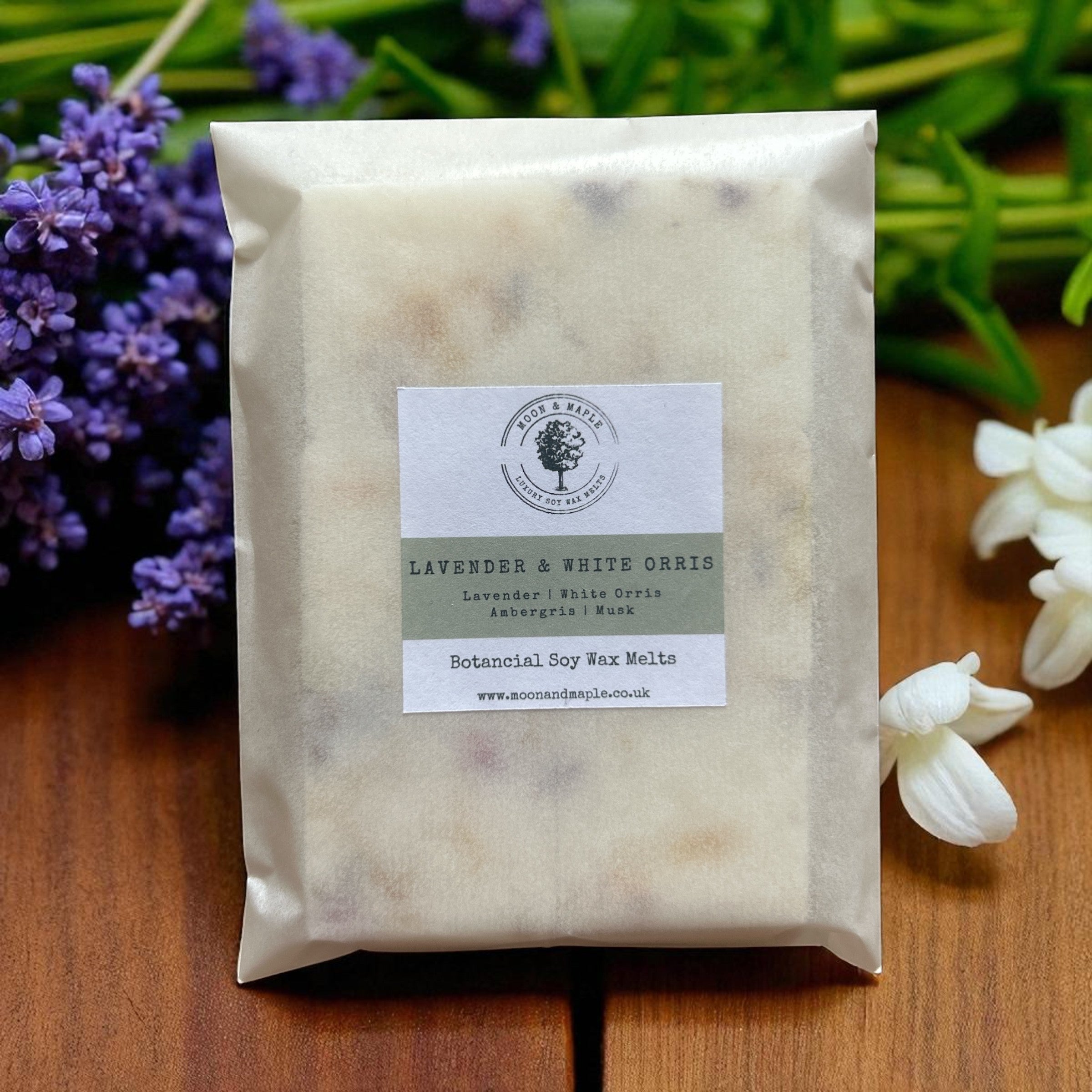 Packaged wax melts with a label on a wooden surface with lavender and white flowers in the background