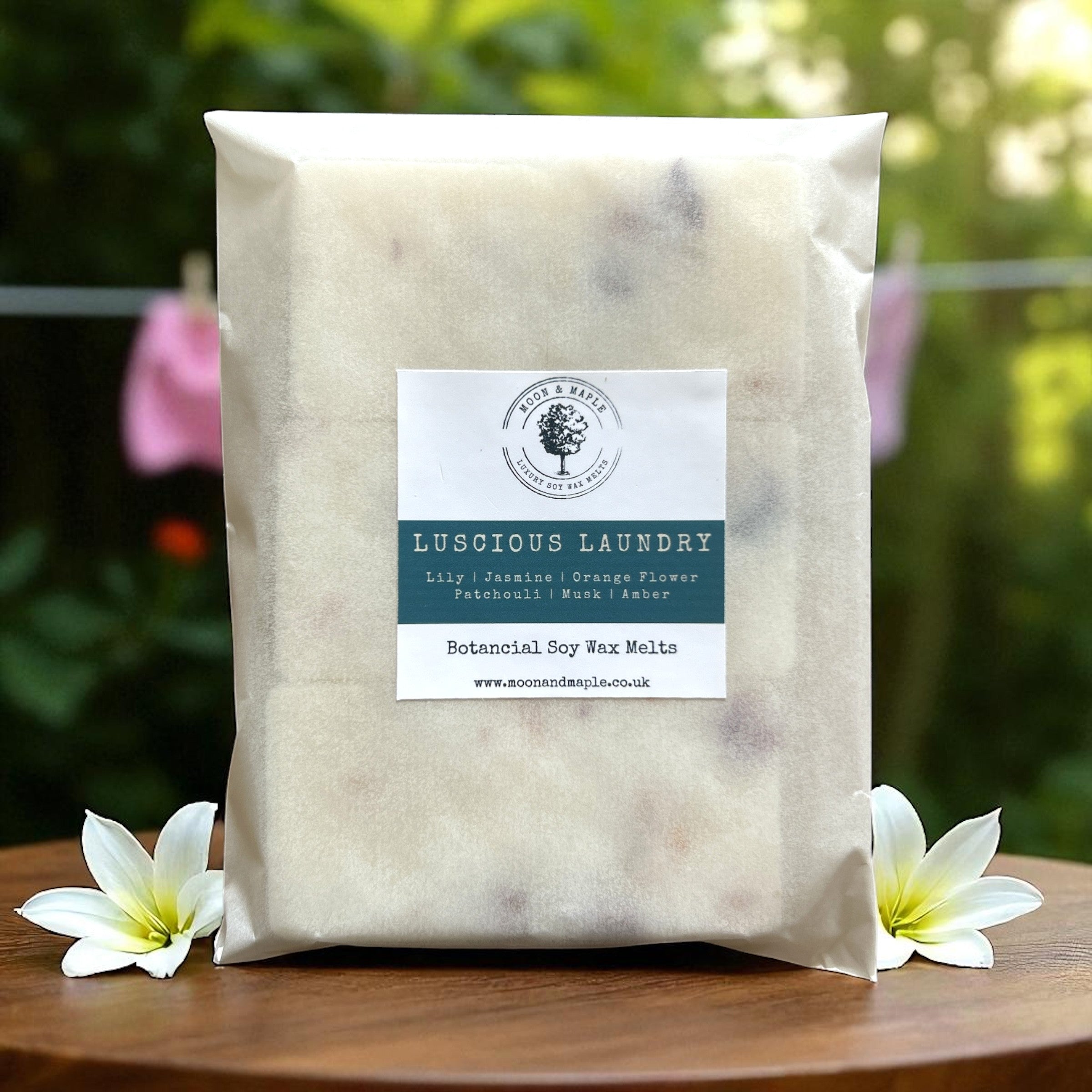 Pack of Luscious Laundry botanical soy wax melts on a wooden surface with flowers and a blurred outdoor background