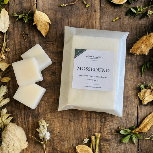 Packaged wax melts with 'Mossbound' label on a wooden surface with dried leaves and herbs.