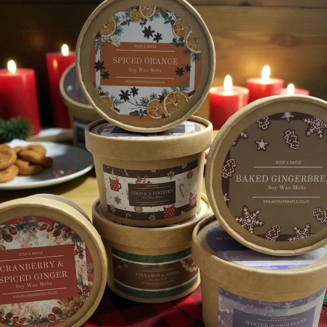 Collection of scented wax melts in decorative tins on a festive tablecloth with candles in the background.